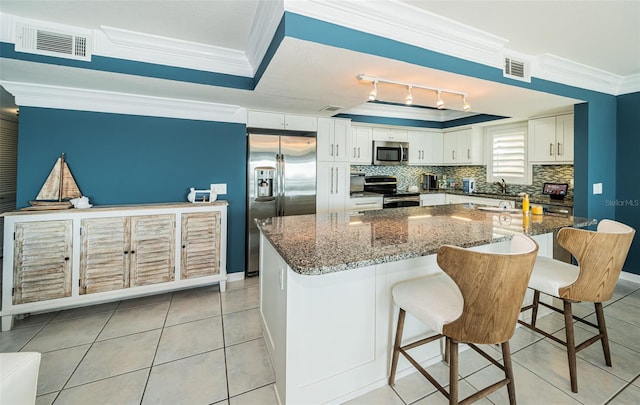 kitchen featuring dark stone counters, ornamental molding, appliances with stainless steel finishes, a kitchen bar, and white cabinetry