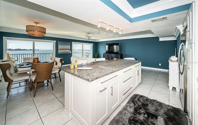 kitchen featuring light tile patterned flooring, ceiling fan, dark stone counters, crown molding, and white cabinetry