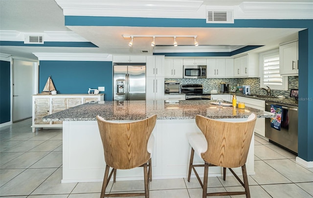 kitchen featuring stainless steel appliances, white cabinets, dark stone countertops, a spacious island, and a kitchen bar