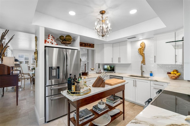 kitchen with sink, a tray ceiling, stainless steel fridge, pendant lighting, and white cabinets