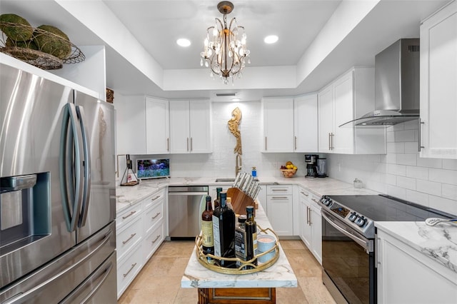 kitchen with white cabinets, appliances with stainless steel finishes, light stone countertops, a tray ceiling, and wall chimney exhaust hood