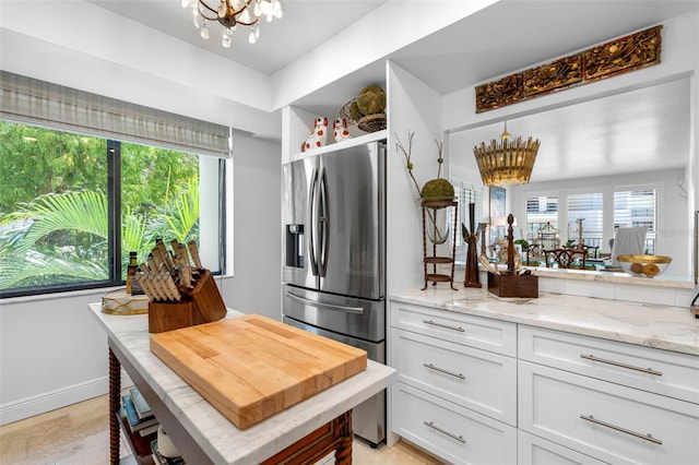 kitchen featuring decorative light fixtures, white cabinets, light stone counters, stainless steel fridge with ice dispenser, and an inviting chandelier