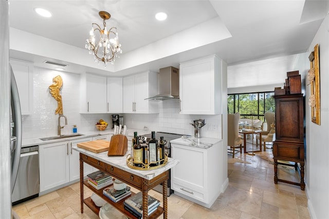 kitchen with a notable chandelier, appliances with stainless steel finishes, white cabinetry, wall chimney exhaust hood, and sink