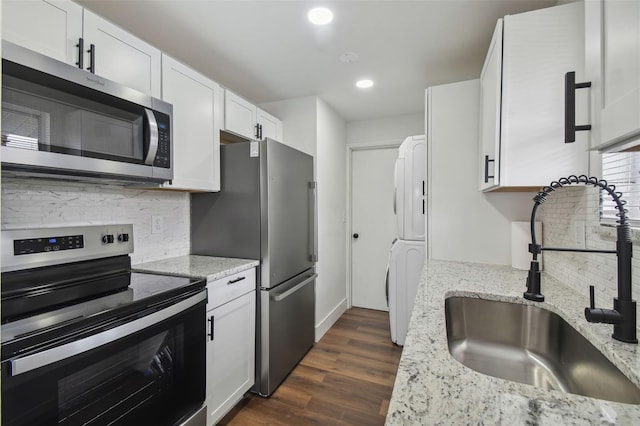 kitchen with sink, white cabinetry, stainless steel appliances, stacked washer and dryer, and dark wood-type flooring