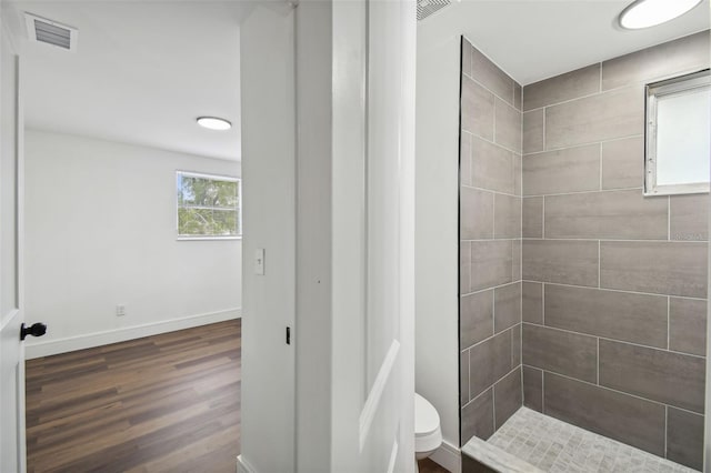 bathroom with toilet, hardwood / wood-style flooring, and tiled shower