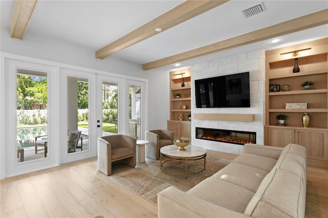 living room featuring beam ceiling, french doors, a tiled fireplace, and light wood-type flooring