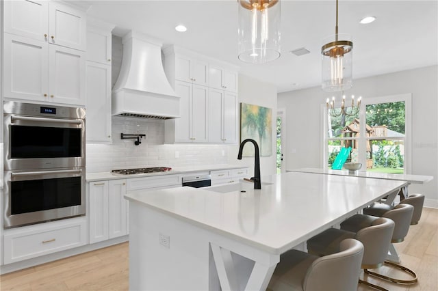 kitchen with custom range hood, light hardwood / wood-style floors, a center island with sink, and white cabinets