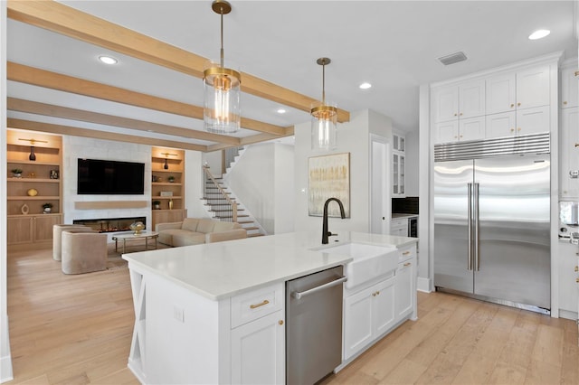 kitchen with an island with sink, hanging light fixtures, stainless steel appliances, sink, and white cabinetry