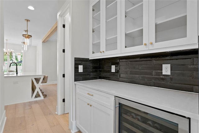 bar featuring decorative backsplash, hanging light fixtures, beverage cooler, white cabinets, and light hardwood / wood-style floors