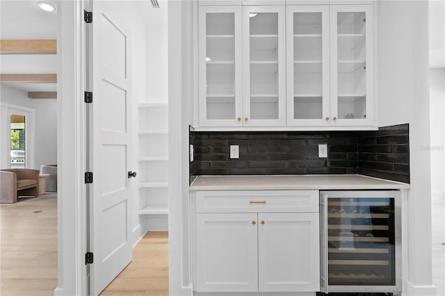 bar featuring wine cooler, decorative backsplash, white cabinets, and light hardwood / wood-style flooring