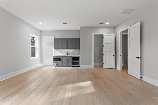 unfurnished living room with wine cooler, sink, and light wood-type flooring