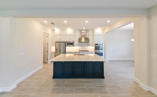 kitchen with a large island, white cabinets, light stone countertops, wall chimney exhaust hood, and stainless steel appliances