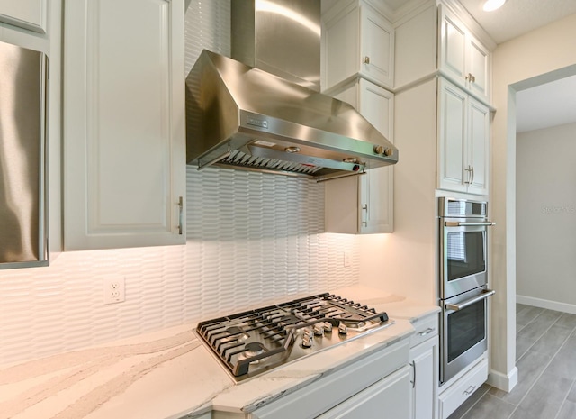 kitchen featuring light stone countertops, white cabinetry, wall chimney range hood, and stainless steel appliances