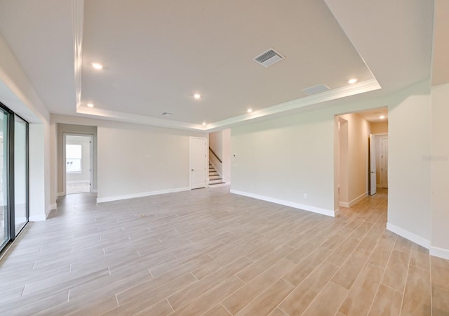 unfurnished room featuring crown molding, a tray ceiling, and light wood-type flooring