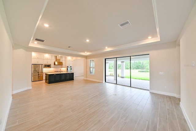 unfurnished living room with light hardwood / wood-style flooring, sink, and a tray ceiling