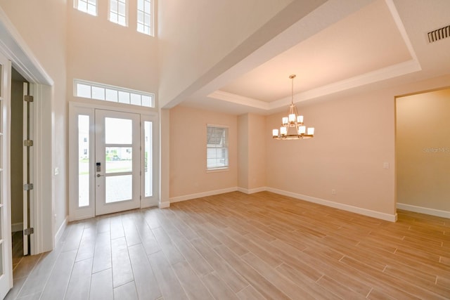 entryway featuring a tray ceiling, light hardwood / wood-style flooring, and an inviting chandelier