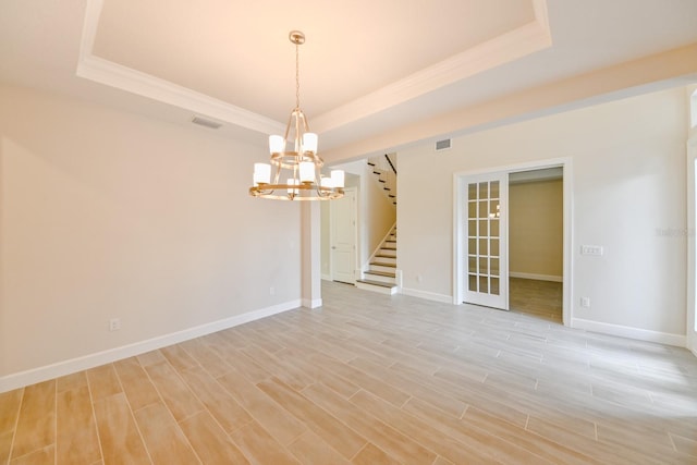 spare room with light hardwood / wood-style flooring, a chandelier, and a raised ceiling