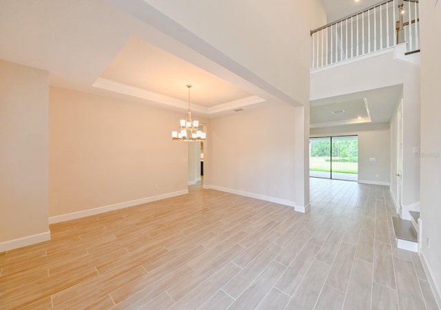 spare room with a notable chandelier, a tray ceiling, and light wood-type flooring