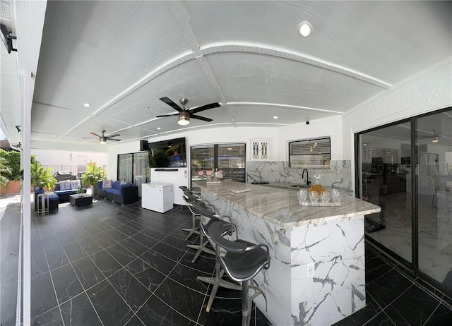 bar with sink, ceiling fan, vaulted ceiling, white cabinets, and light stone counters