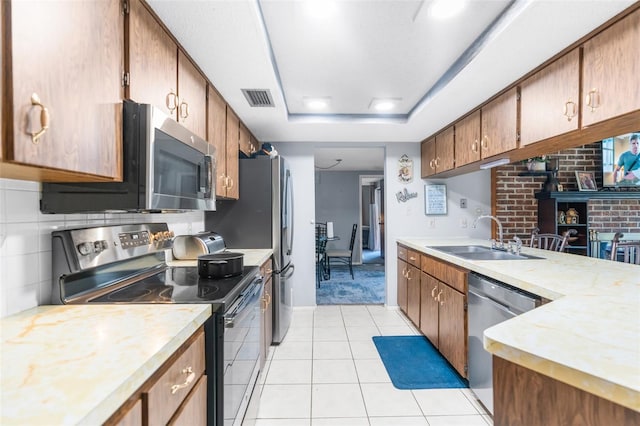 kitchen featuring appliances with stainless steel finishes, a tray ceiling, sink, and light tile patterned floors