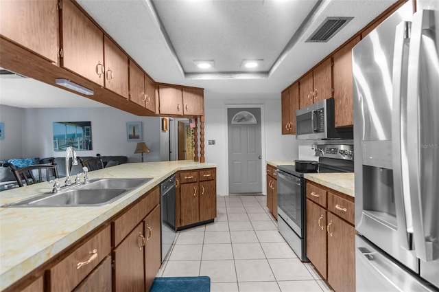 kitchen with a raised ceiling, appliances with stainless steel finishes, sink, and light tile patterned floors