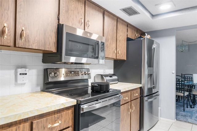 kitchen with a raised ceiling, appliances with stainless steel finishes, light tile patterned floors, and backsplash