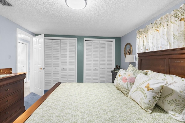 bedroom featuring light carpet, a textured ceiling, and multiple closets