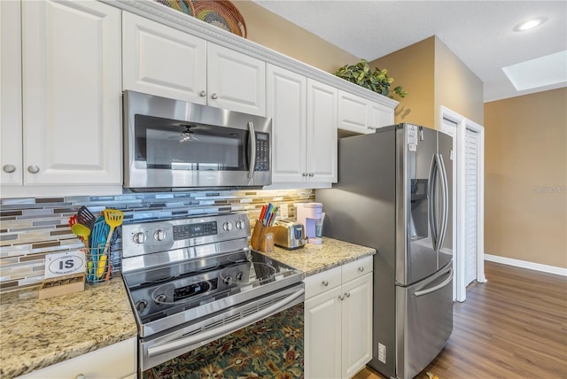 kitchen with decorative backsplash, white cabinets, appliances with stainless steel finishes, light stone countertops, and wood-type flooring