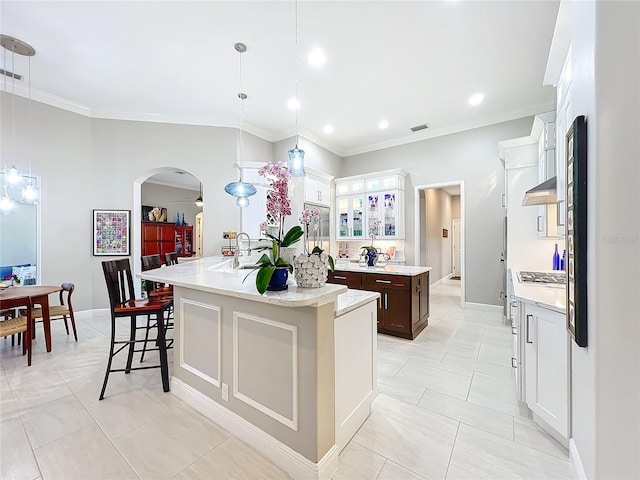 kitchen featuring white cabinetry, a breakfast bar, decorative light fixtures, and an island with sink