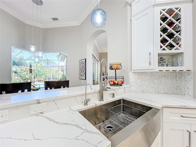 kitchen featuring light stone counters, white cabinetry, ornamental molding, sink, and decorative light fixtures