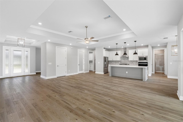 unfurnished living room with ornamental molding, ceiling fan, light hardwood / wood-style floors, and a raised ceiling