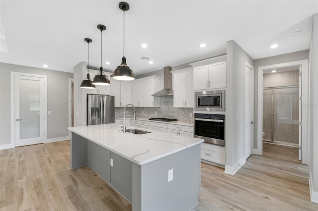 kitchen featuring a kitchen island with sink, sink, wall chimney range hood, white cabinetry, and appliances with stainless steel finishes