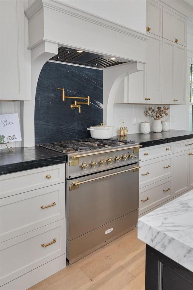 kitchen featuring premium range hood, white cabinetry, gas range oven, decorative backsplash, and light wood-type flooring