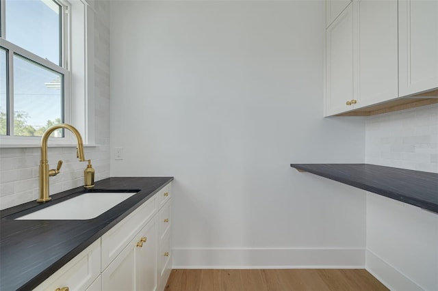 bar featuring sink, decorative backsplash, white cabinets, and light wood-type flooring