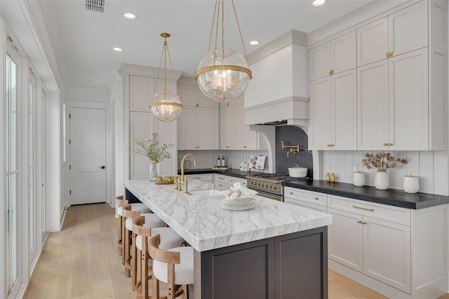 kitchen with an island with sink, sink, white cabinets, and high end range