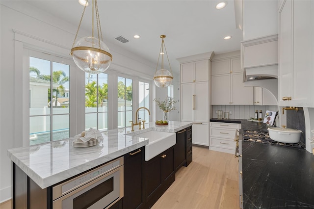 kitchen featuring sink, white cabinetry, stainless steel microwave, an island with sink, and decorative light fixtures