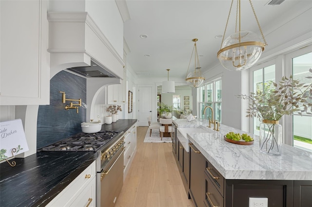 kitchen featuring decorative light fixtures, light stone countertops, a kitchen island with sink, and high end stove