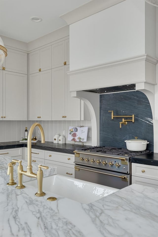 kitchen featuring tasteful backsplash, dark stone countertops, stainless steel stove, and white cabinets