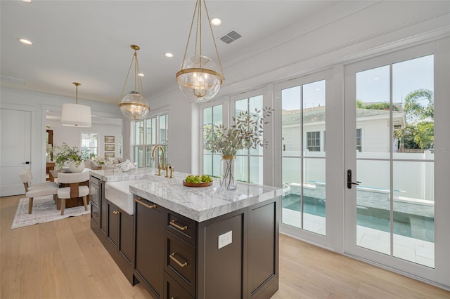 kitchen with a kitchen island with sink, sink, decorative light fixtures, and light wood-type flooring