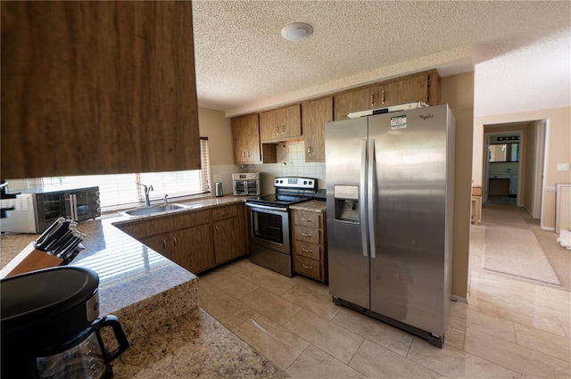 kitchen with brown cabinets, backsplash, appliances with stainless steel finishes, a sink, and a textured ceiling