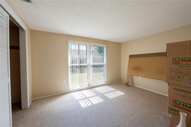 carpeted spare room with a textured ceiling and baseboards