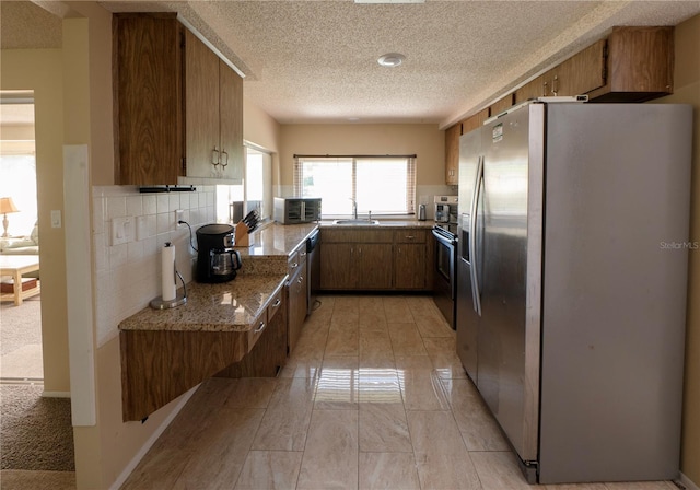 kitchen featuring brown cabinets, a sink, stainless steel appliances, a textured ceiling, and backsplash