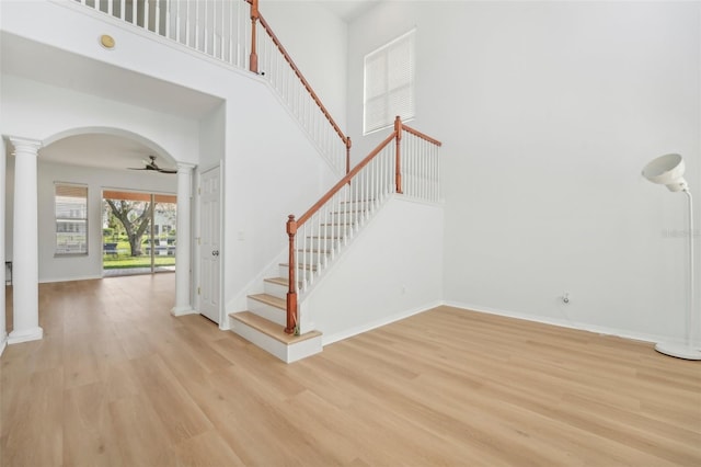 foyer entrance with decorative columns, light hardwood / wood-style floors, a towering ceiling, and ceiling fan