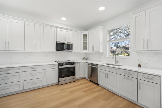 kitchen with white cabinets, backsplash, appliances with stainless steel finishes, light hardwood / wood-style flooring, and sink