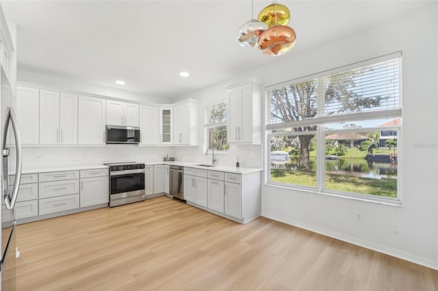 kitchen featuring hanging light fixtures, white cabinetry, sink, light hardwood / wood-style floors, and stainless steel appliances