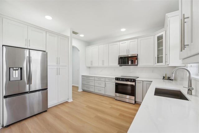 18051 Java Isle Dr, Tampa, FL 33647 - kitchen featuring stainless steel appliances, a sink, arched walkways, white cabinets, and light wood-style floors