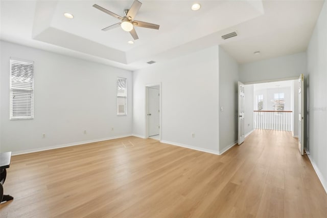 spare room with a raised ceiling, light wood-type flooring, and ceiling fan