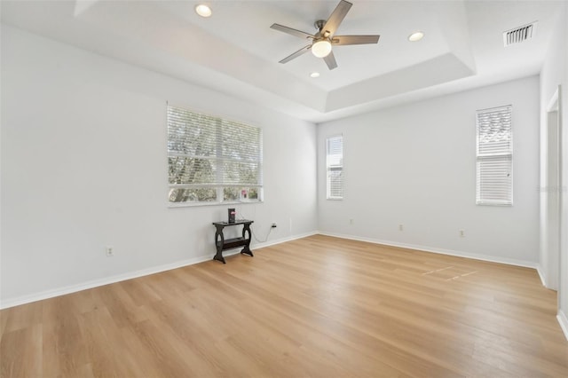 unfurnished room featuring light hardwood / wood-style flooring, ceiling fan, and a raised ceiling