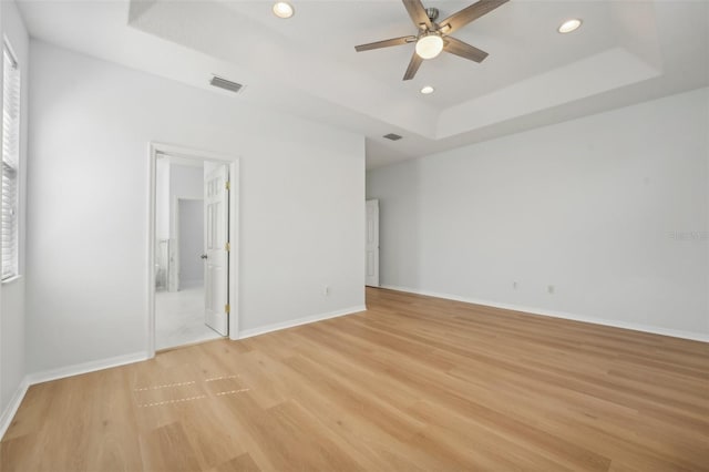 unfurnished bedroom with a tray ceiling, light wood-type flooring, and ceiling fan