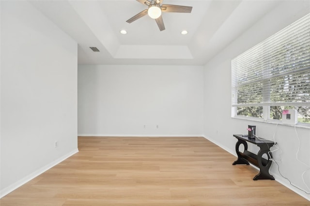 spare room featuring a tray ceiling, light wood-type flooring, and ceiling fan